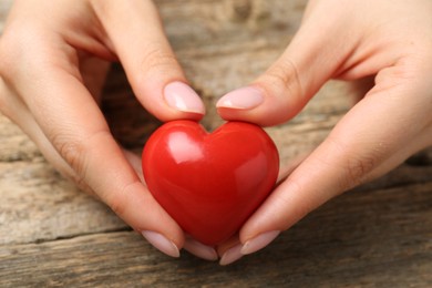 Photo of Woman with red decorative heart at wooden table, closeup