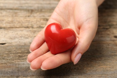 Photo of Woman with red decorative heart at wooden table, closeup