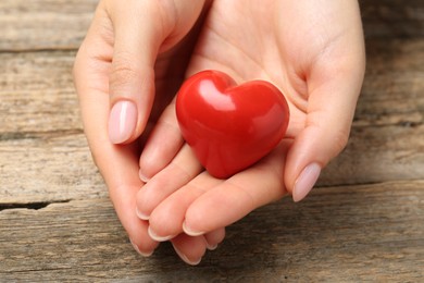 Photo of Woman with red decorative heart at wooden table, closeup