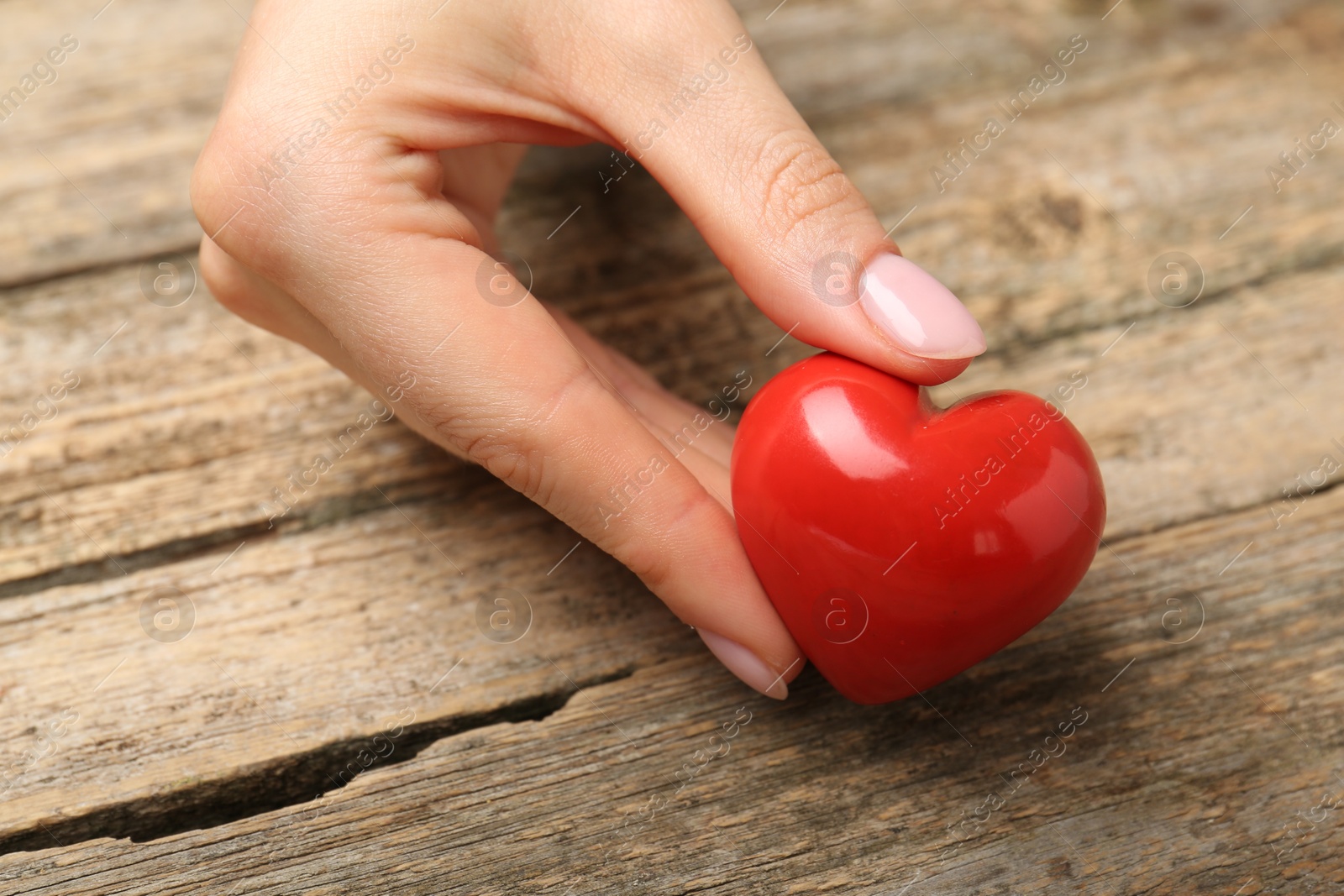 Photo of Woman with red decorative heart at wooden table, closeup