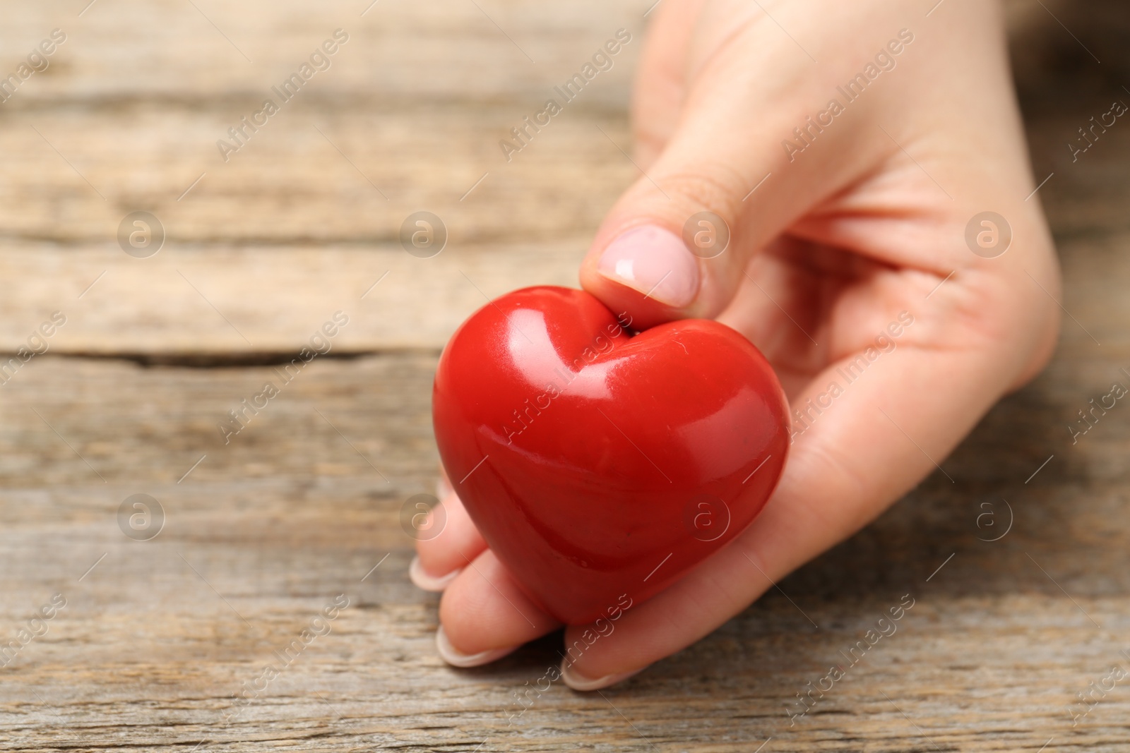 Photo of Woman with red decorative heart at wooden table, closeup. Space for text