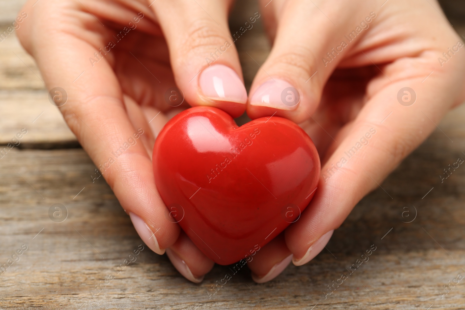 Photo of Woman with red decorative heart at wooden table, closeup