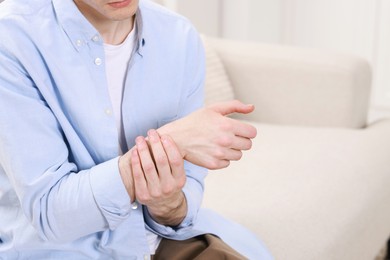 Man suffering from pain in hand on sofa indoors, closeup. Space for text