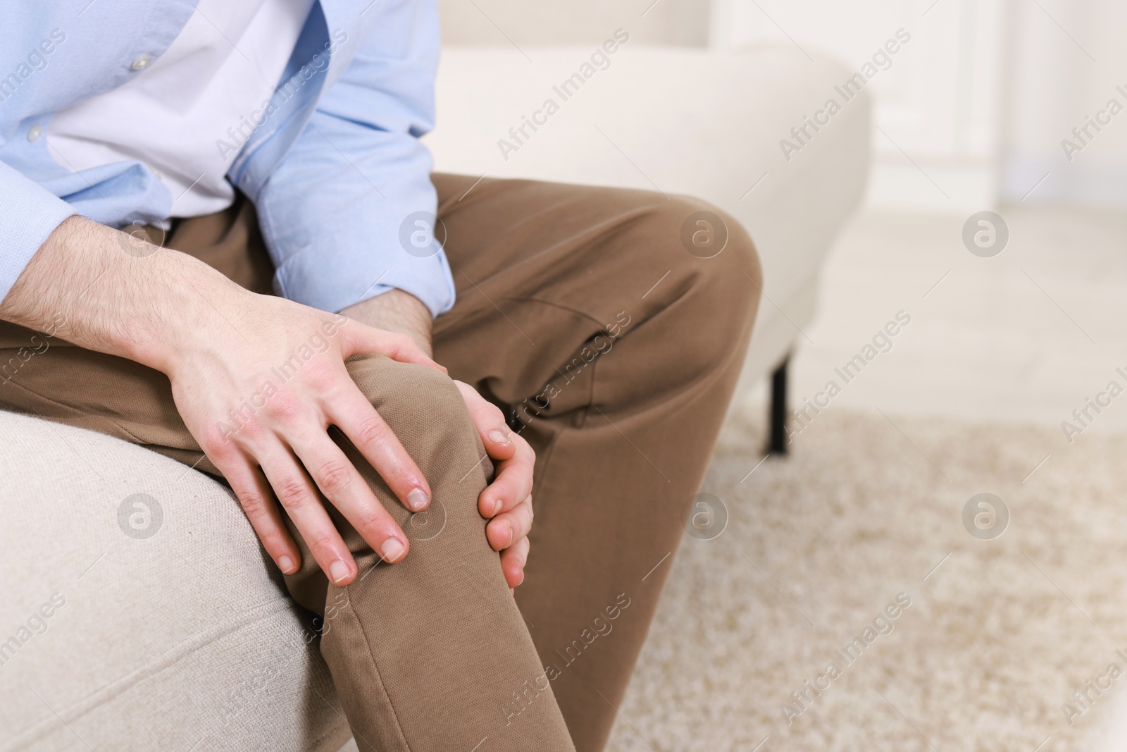 Photo of Man suffering from knee pain on sofa indoors, closeup. Space for text