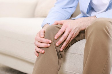 Photo of Man suffering from knee pain on sofa indoors, closeup