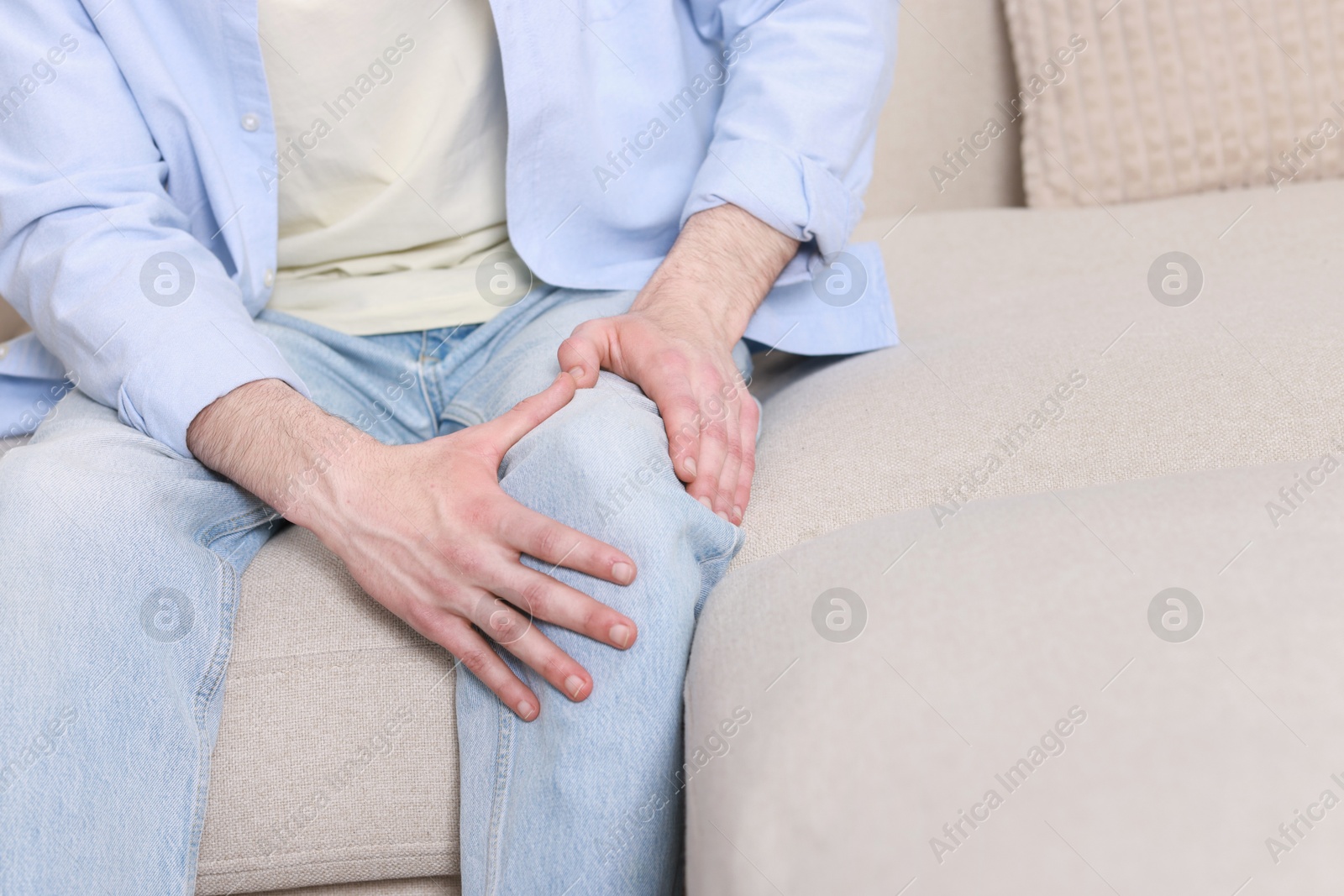 Photo of Man suffering from knee pain on sofa indoors, closeup