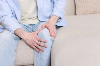 Man suffering from knee pain on sofa indoors, closeup