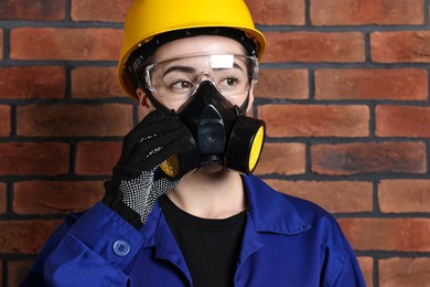 Photo of Worker in respirator, protective glasses and helmet near brick wall