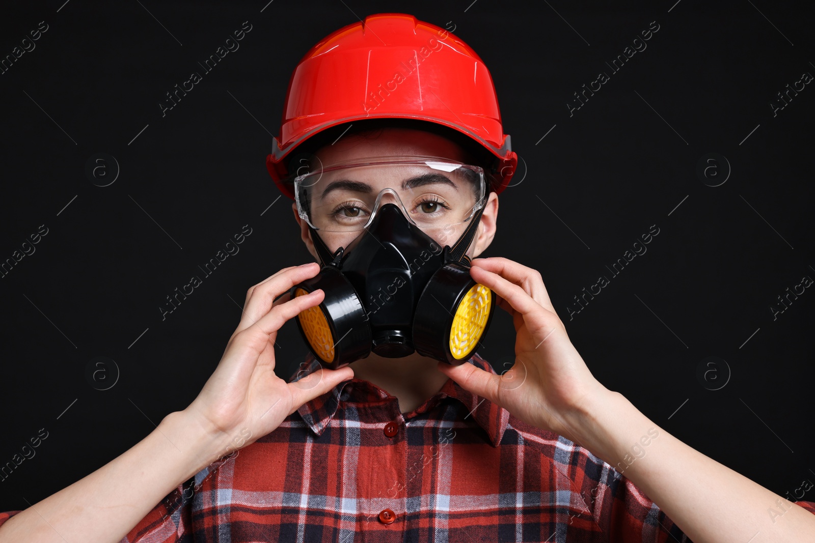 Photo of Woman in respirator, protective glasses and helmet on black background