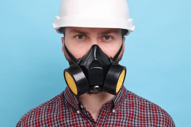 Man in respirator mask and hard hat on light blue background