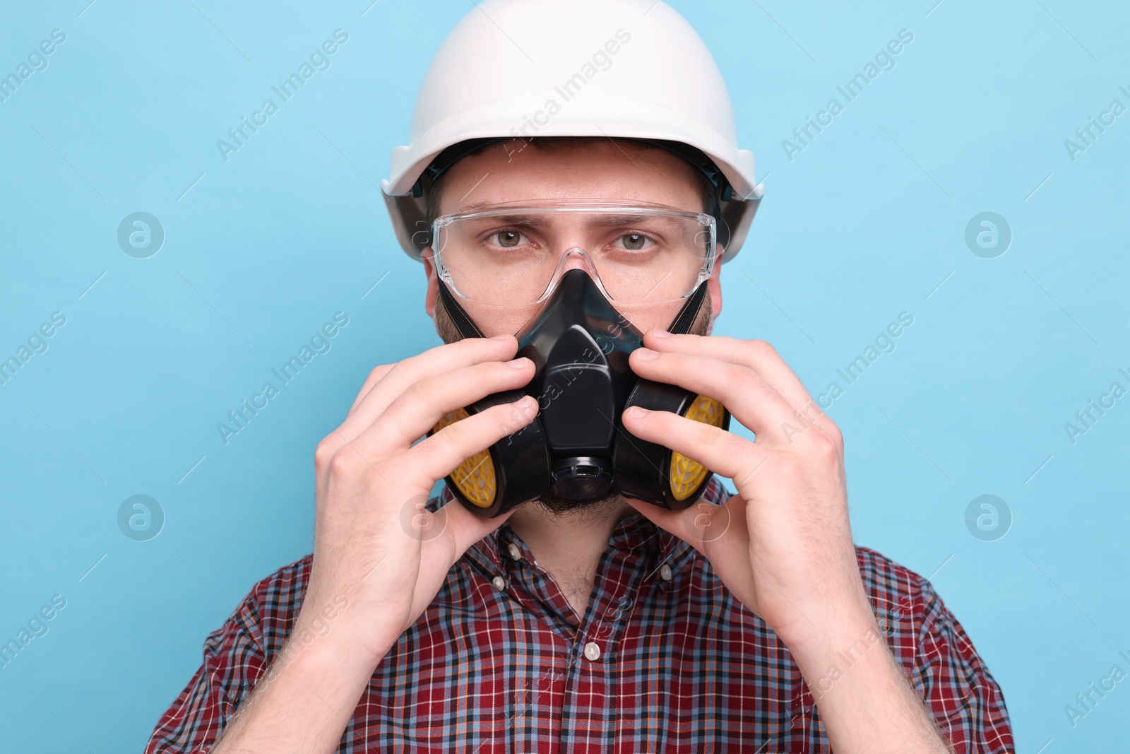 Photo of Man in respirator mask and hard hat on light blue background