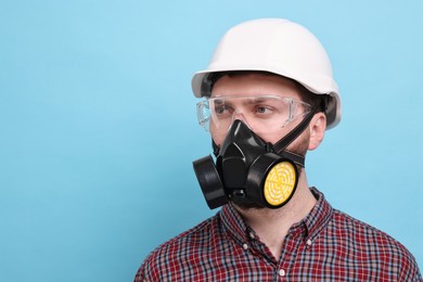 Man in respirator mask and hard hat on light blue background. Space for text