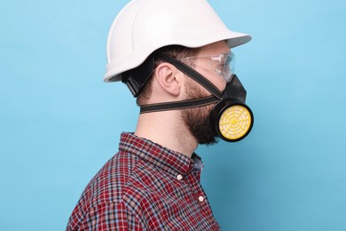 Photo of Man in respirator mask and hard hat on light blue background