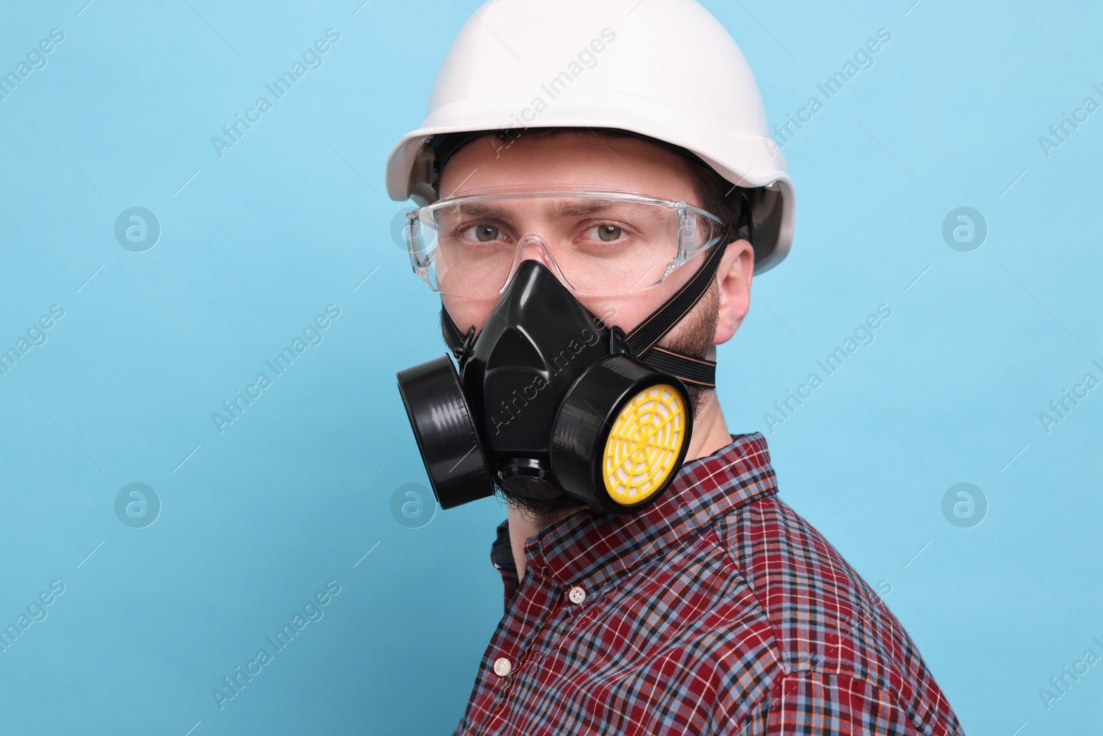 Photo of Man in respirator mask and hard hat on light blue background