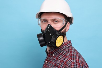 Man in respirator mask and hard hat on light blue background