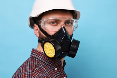 Man in respirator mask and hard hat on light blue background