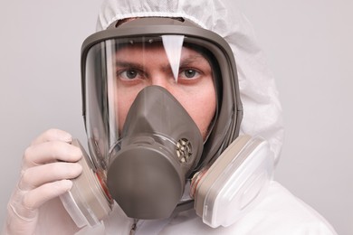 Man wearing protective suit with respirator mask on light background