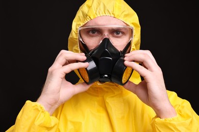 Man wearing protective suit with respirator mask on black background