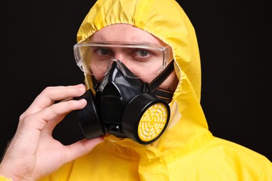 Man wearing protective suit with respirator mask on black background