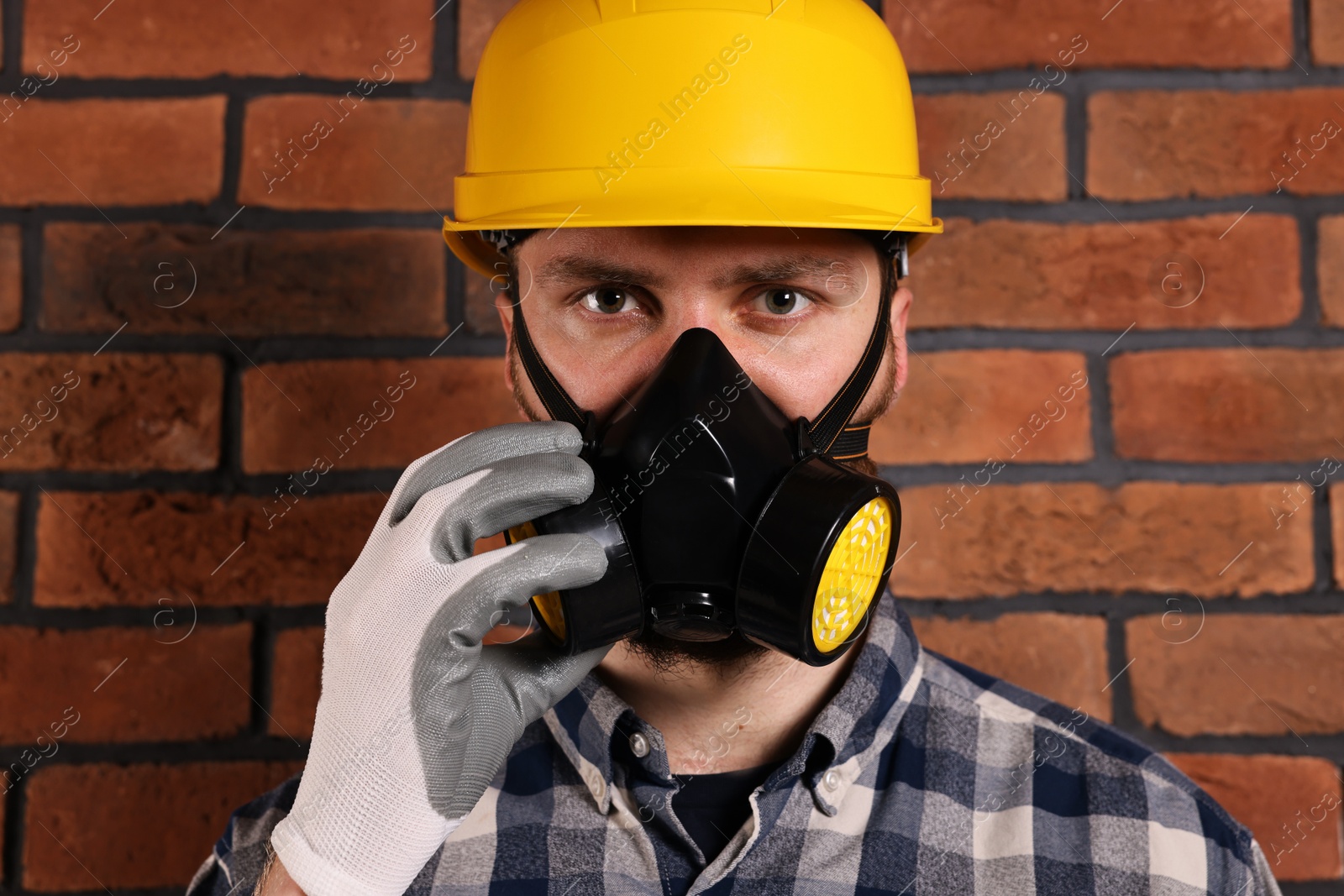 Photo of Man in respirator mask and hard hat near red brick wall