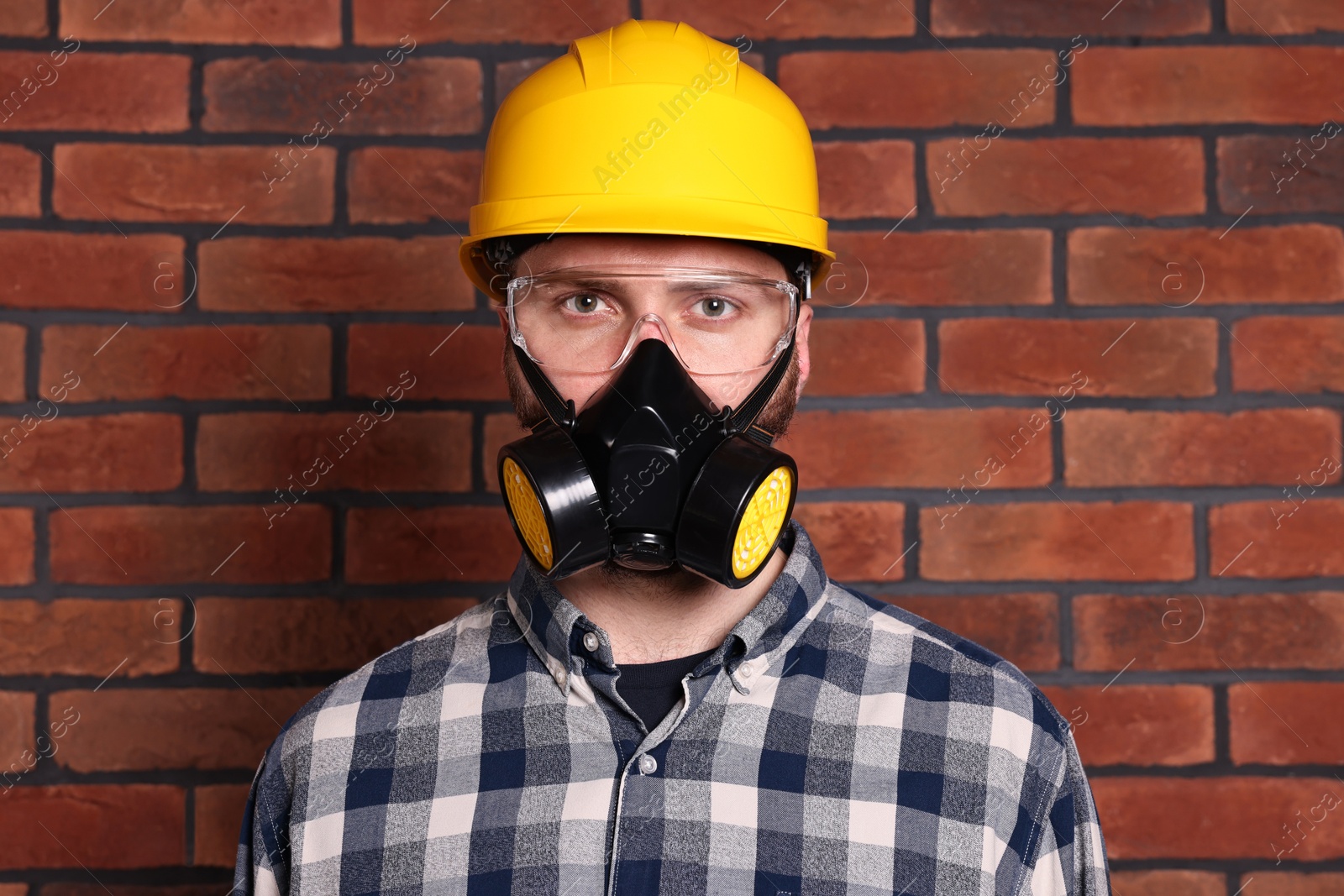 Photo of Man in respirator mask and hard hat near red brick wall