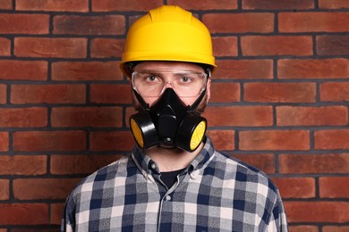 Photo of Man in respirator mask and hard hat near red brick wall