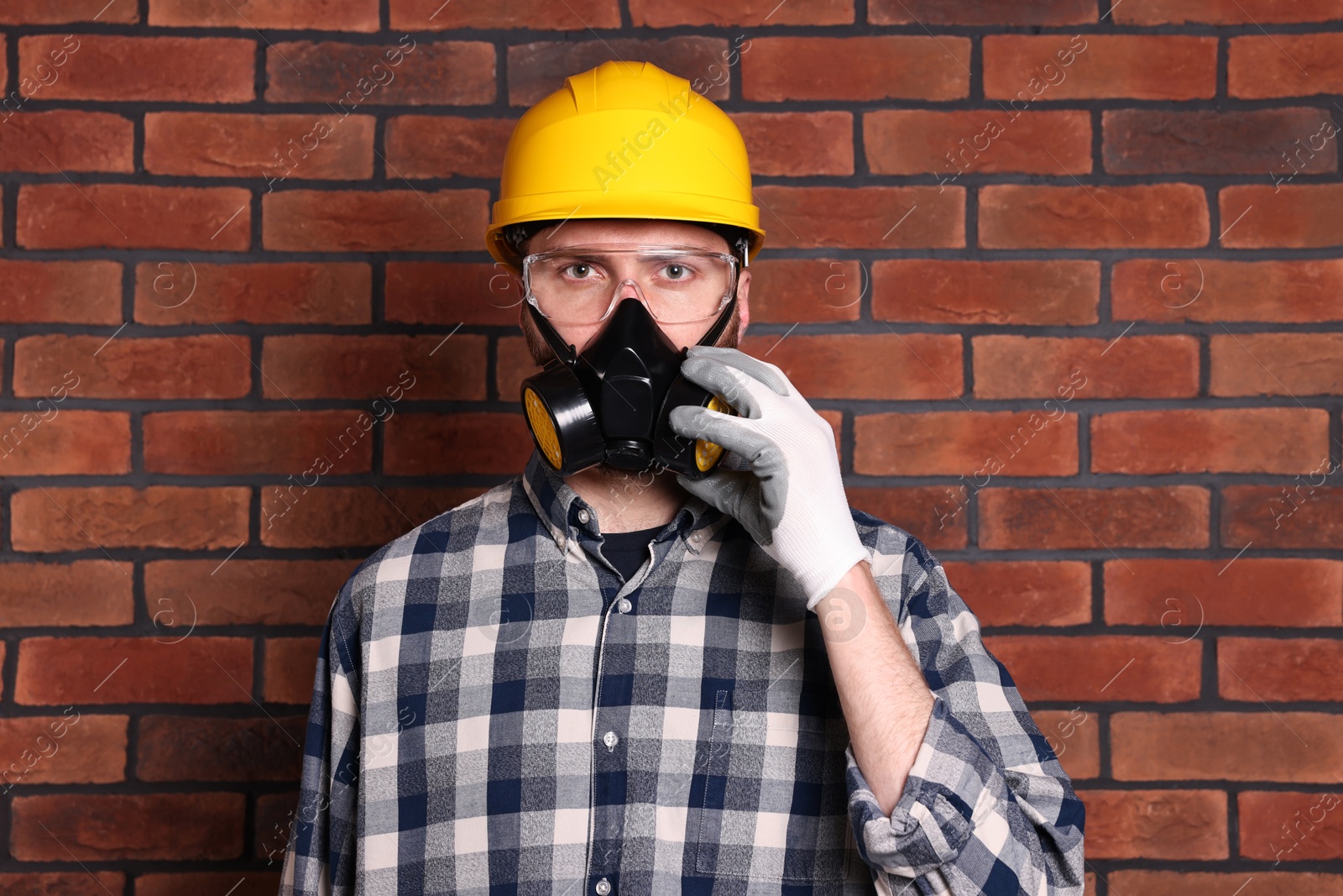 Photo of Man in respirator mask and hard hat near red brick wall. Space for text