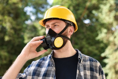 Photo of Man in respirator mask and hard hat outdoors. Safety equipment