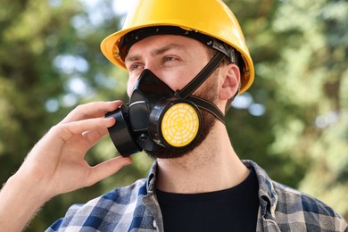 Photo of Man in respirator mask and hard hat outdoors. Safety equipment