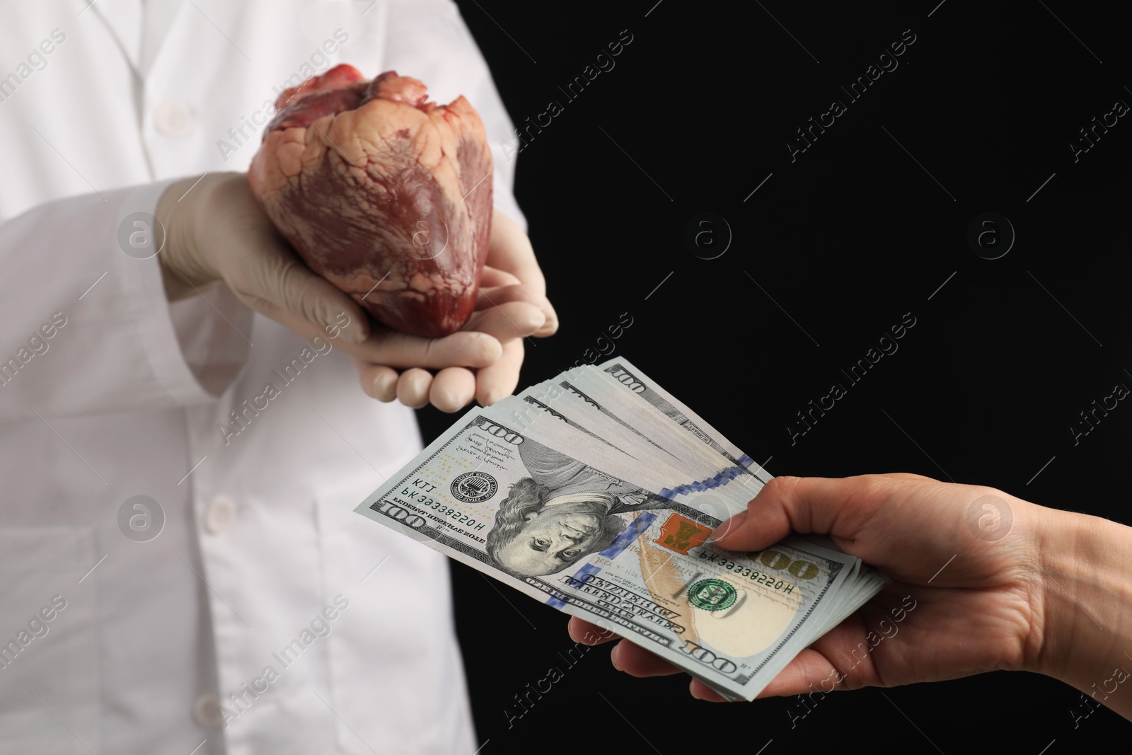 Photo of Patient giving dollar banknotes to doctor with heart on black background, closeup