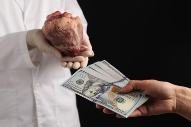 Patient giving dollar banknotes to doctor with heart on black background, closeup