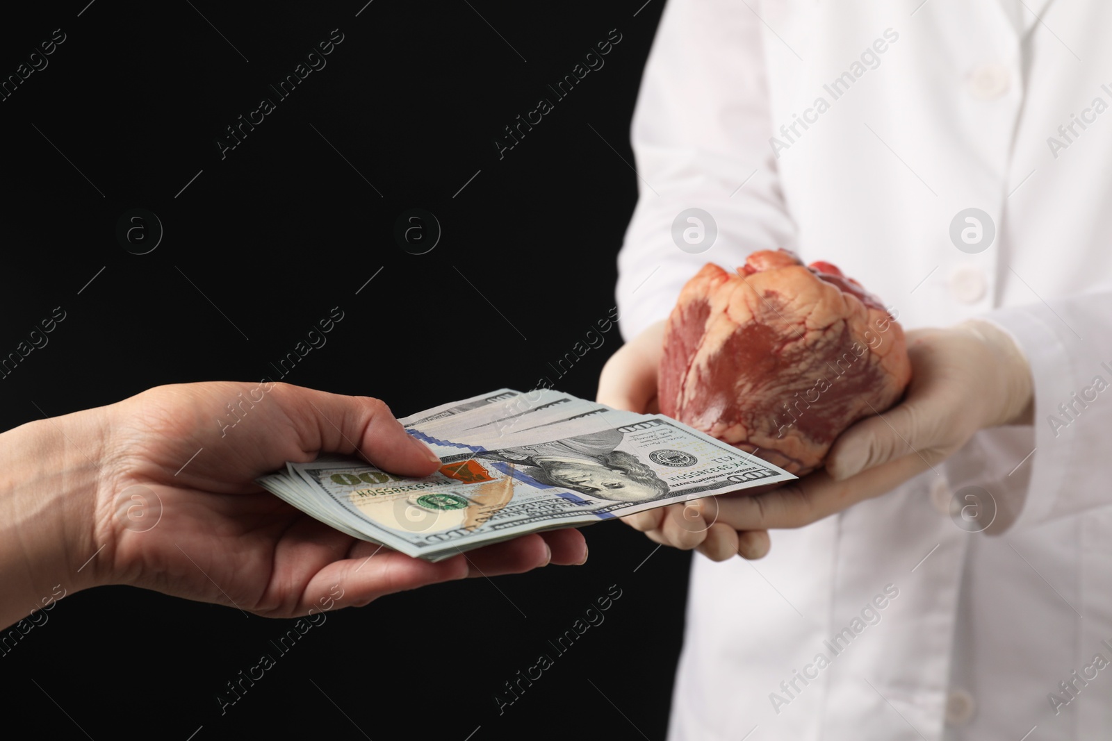 Photo of Patient giving dollar banknotes to doctor with heart on black background, closeup