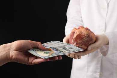 Patient giving dollar banknotes to doctor with heart on black background, closeup