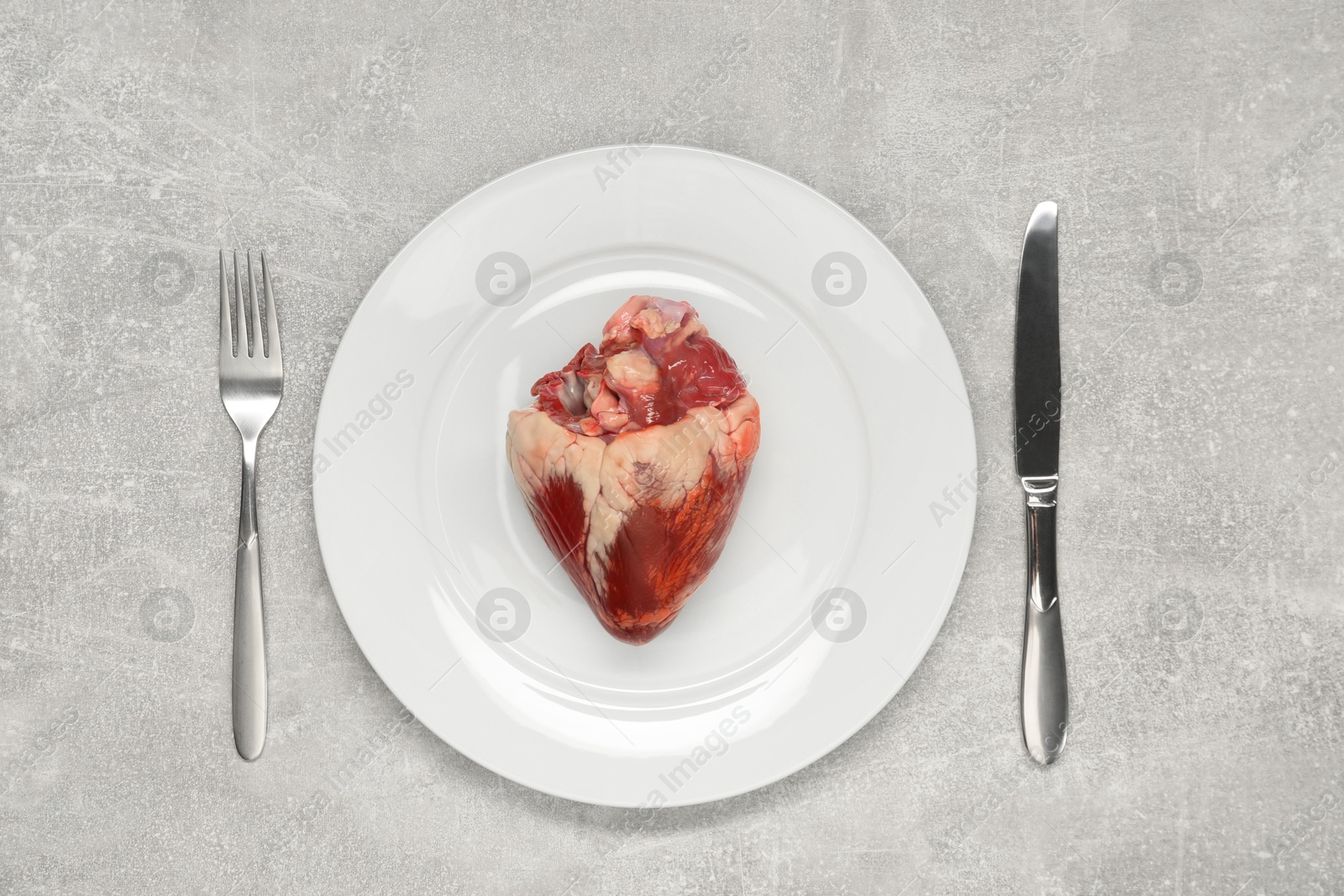 Photo of Raw heart, fork and knife on grey table, top view