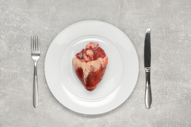 Photo of Raw heart, fork and knife on grey table, top view