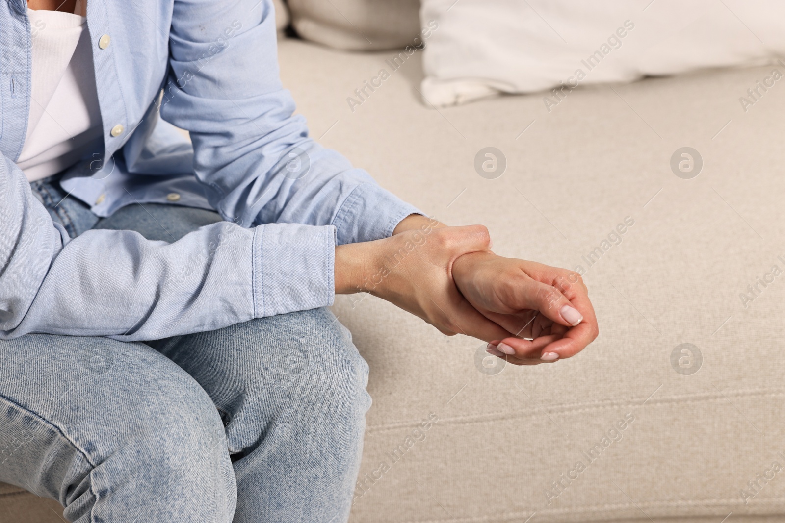 Photo of Woman suffering from pain in wrist on sofa indoors, closeup