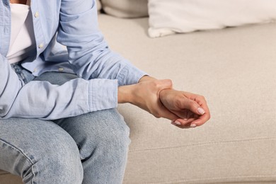 Woman suffering from pain in wrist on sofa indoors, closeup