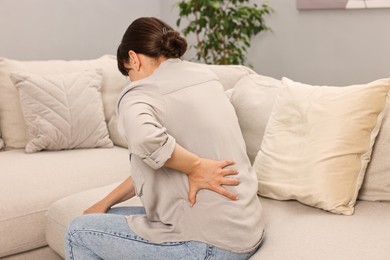 Photo of Woman suffering from back pain on sofa at home
