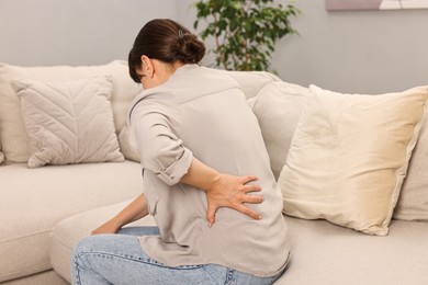 Woman suffering from back pain on sofa at home