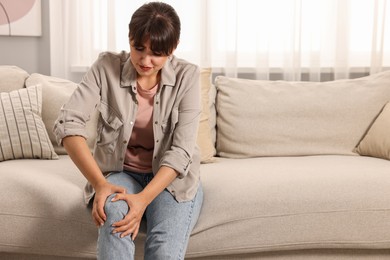 Photo of Upset woman suffering from knee pain on sofa at home