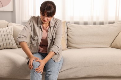 Upset woman suffering from knee pain on sofa at home