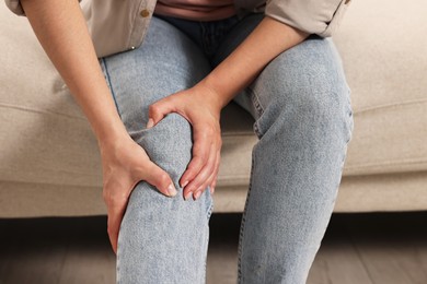 Photo of Woman suffering from knee pain on sofa indoors, closeup