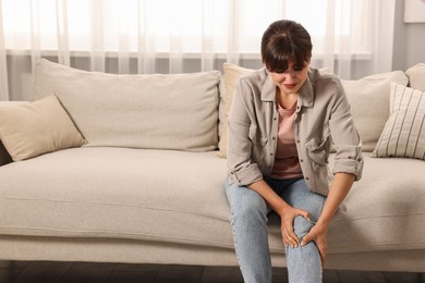 Upset woman suffering from knee pain on sofa at home