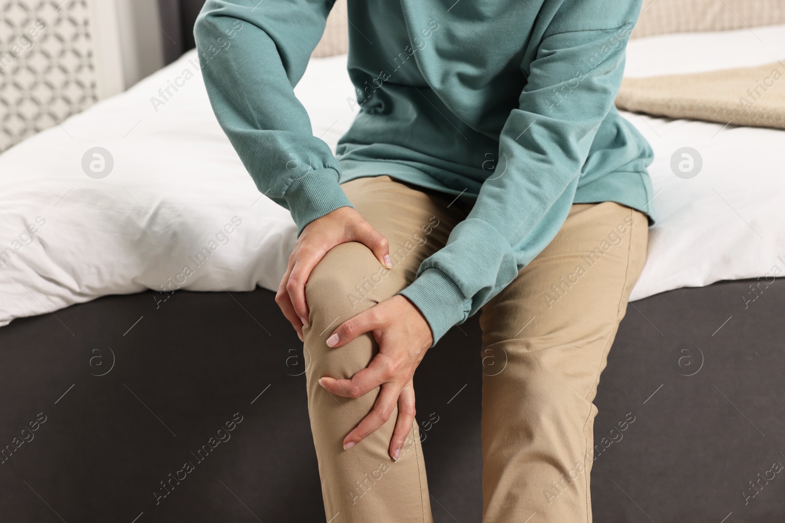 Photo of Woman suffering from knee pain on bed at home, closeup