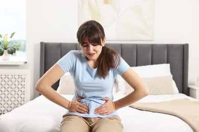 Upset woman suffering from abdominal pain on bed at home