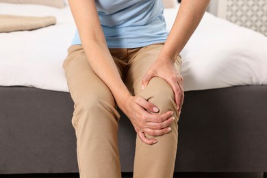 Photo of Woman suffering from knee pain on bed at home, closeup