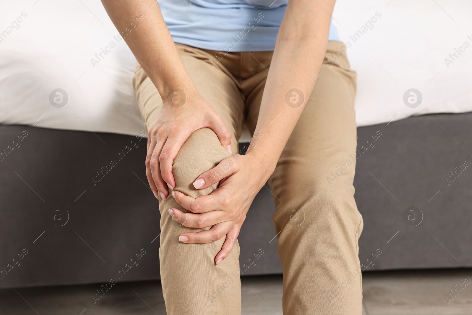 Photo of Woman suffering from knee pain on bed at home, closeup