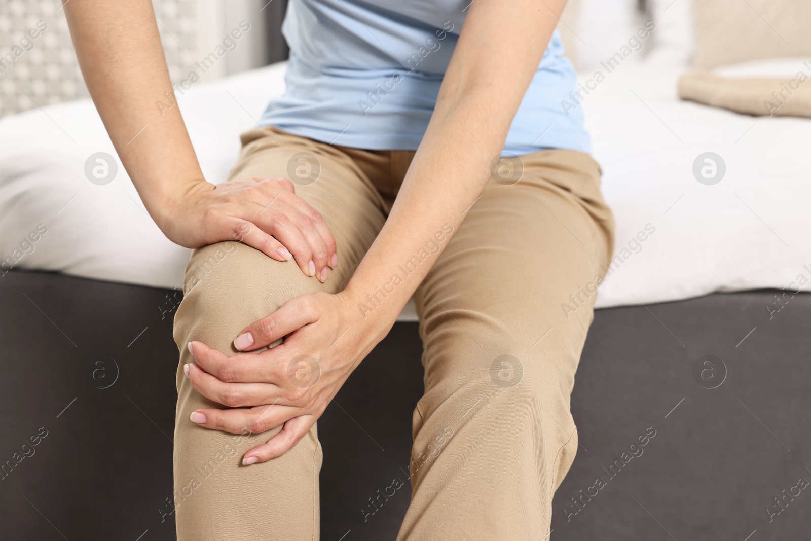 Photo of Woman suffering from knee pain on bed at home, closeup