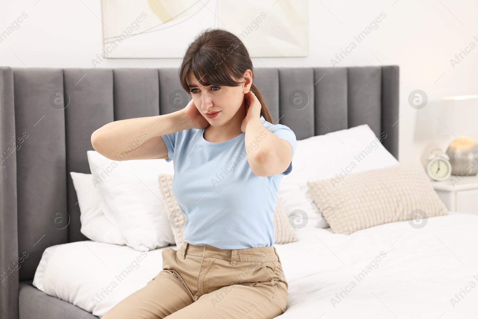 Photo of Upset woman suffering from neck pain on bed at home