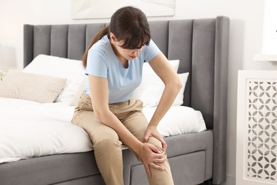 Photo of Woman suffering from knee pain on bed at home